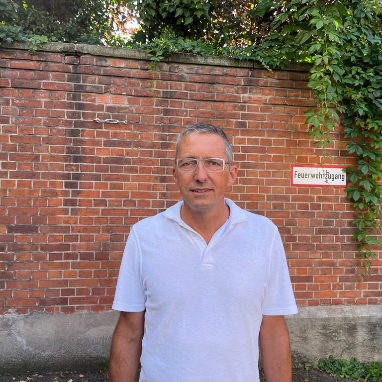 Mann mit grauen Haaren im weißen T-Shirt vor Backsteinmauer. (Foto: SWR)
