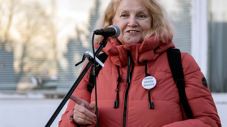 Die Gründerin von „Omas gegen Rechts” Anna Ohnweiler ist bei einer Demonstration und steht auf einer Bühne. Sie steht an einem Mikrofon und schaut in die Kamera. (Foto: Anna Ohnweiler)