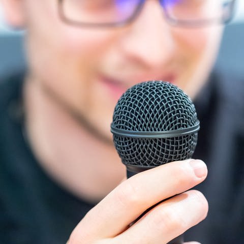 Junger Mann hält Mikrofon vor dem Gesicht: Wenn man in ein Mikrofon spricht, kommt beim Mikrofon der Schall nur über die Luftleitung an – nicht über die Knochenleitung. Deshalb klingt es so anders.  (Foto: picture-alliance / Reportdienste, Picture Alliance)